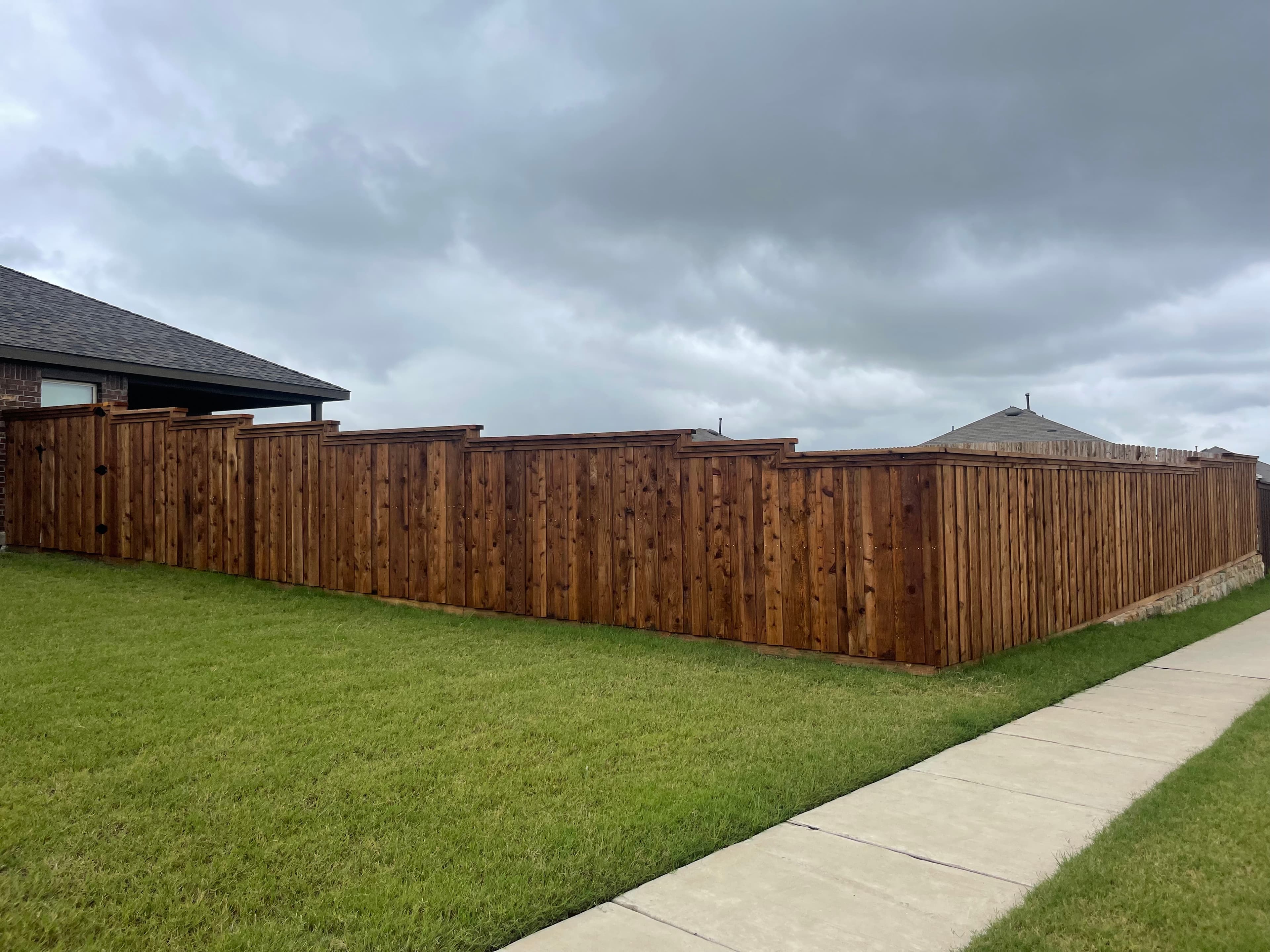 Long brown wooden fence surrounding a yard with green grass