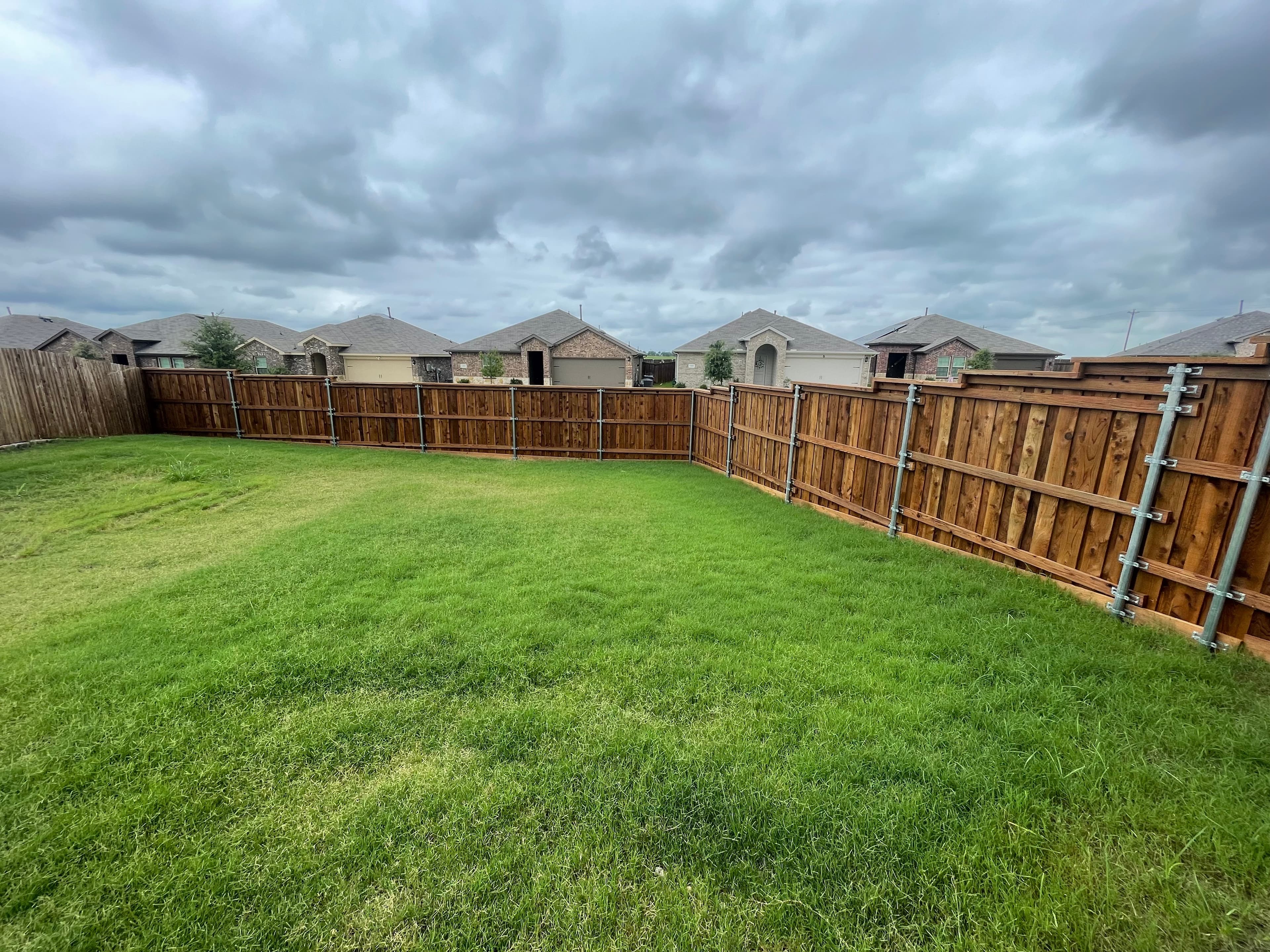 Wooden fence with metal posts enclosing a large backyard