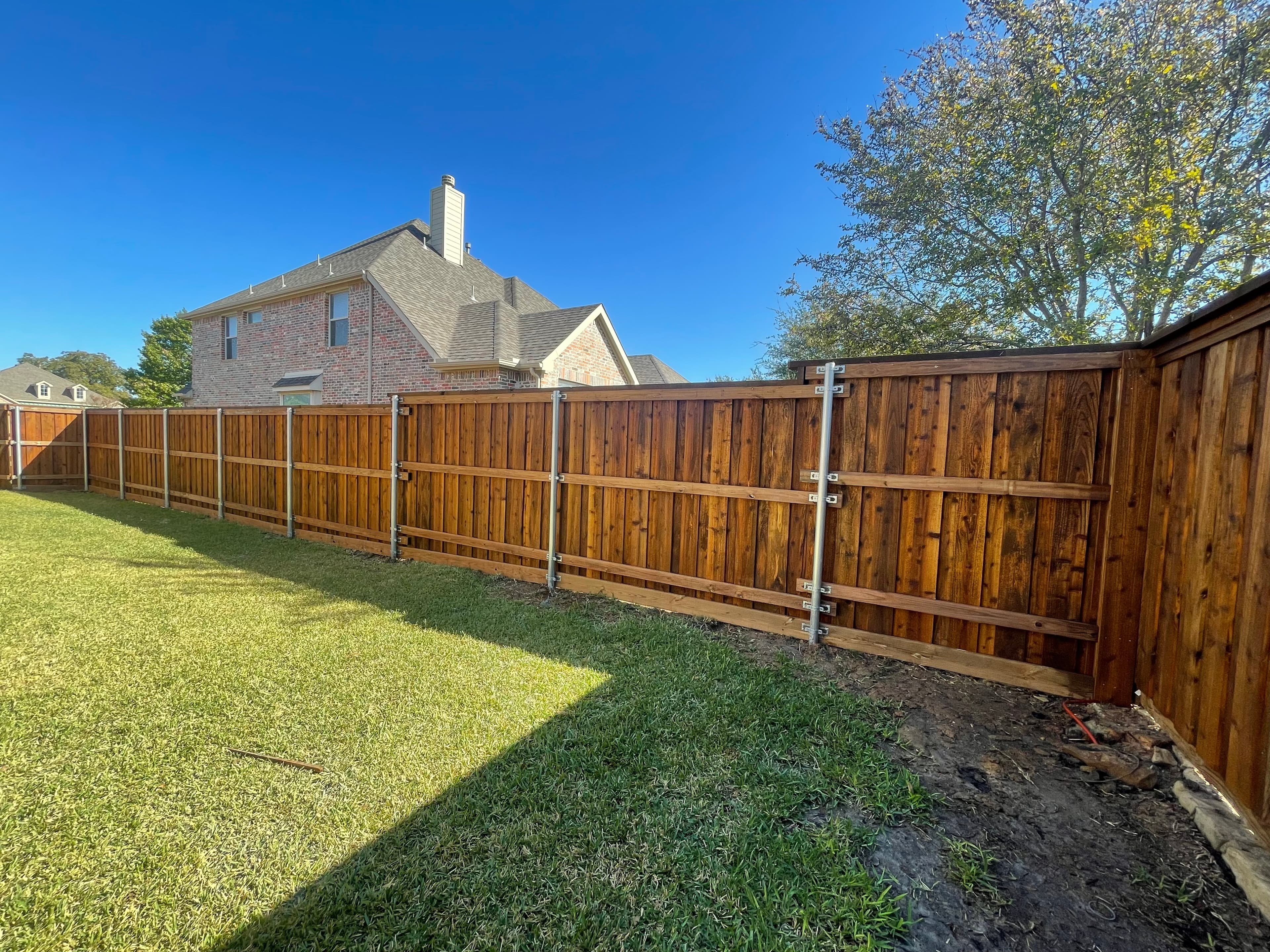Stained wooden fence with metal posts on sunny day